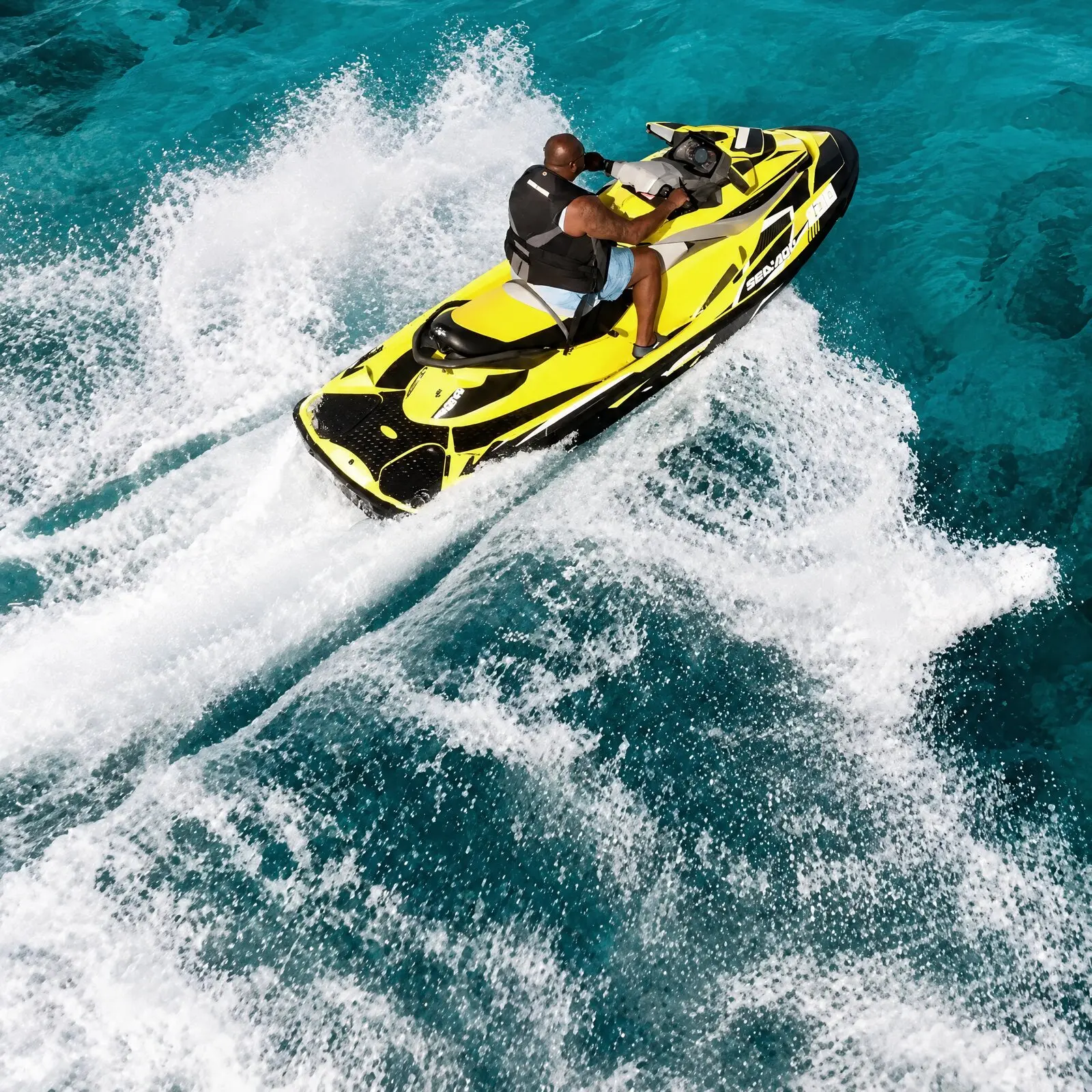 Deux personnes sur un jet ski jaune qui vire dans une gerbe d'écume, vu d'en haut