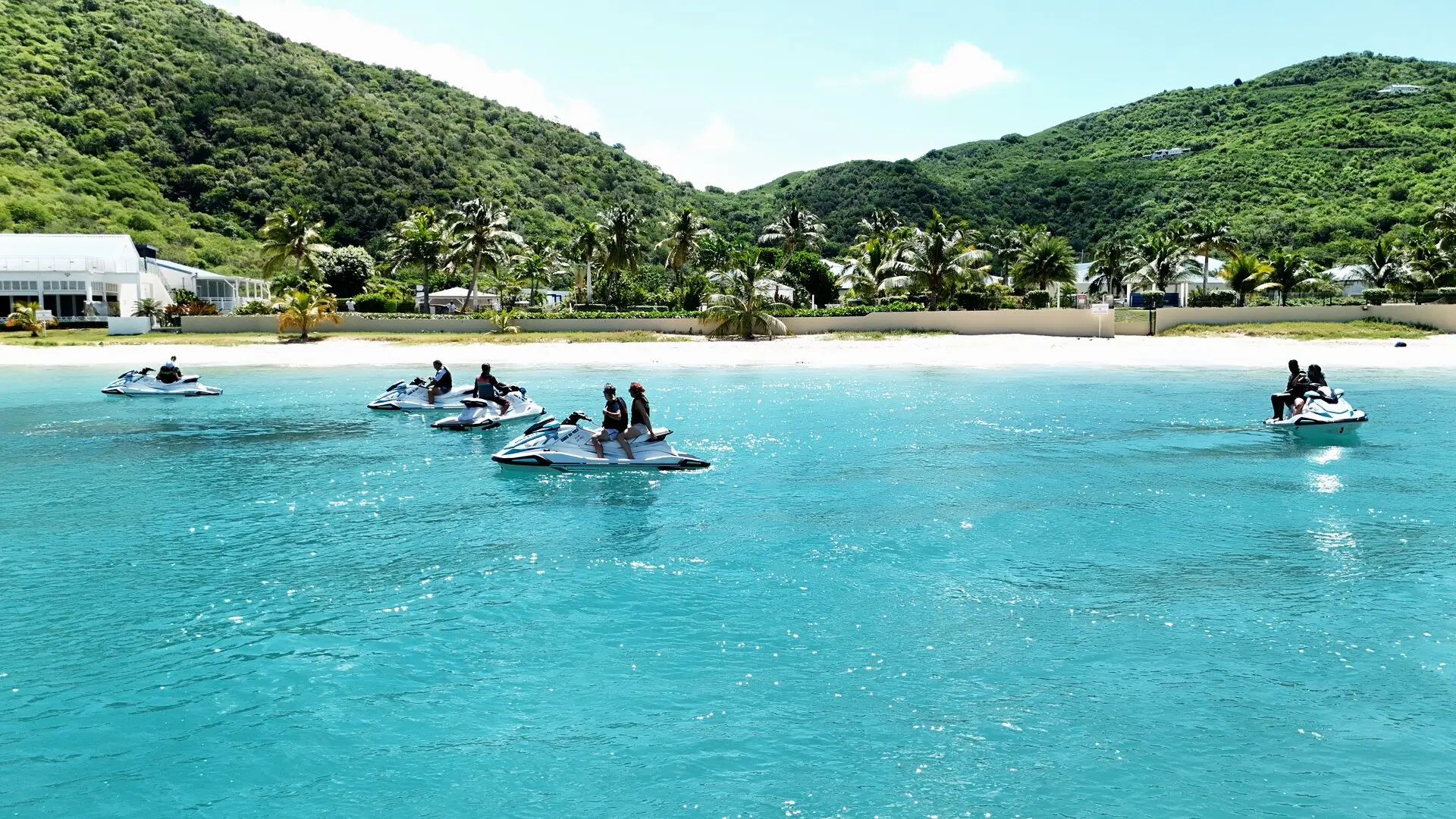 Des jet skis arrêtés sur l'eau turquoise devant la plage d'Anse Marcel, les collines derrière