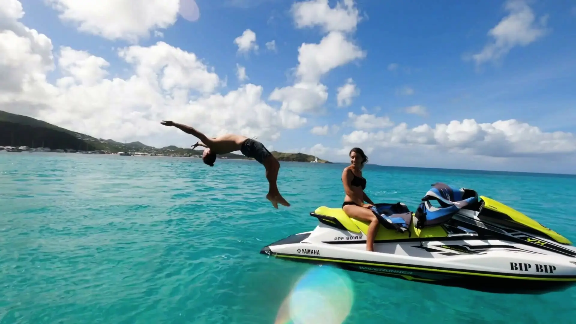 Salto arrière depuis un jet ski jaune sur l'eau turquoise de Saint-Martin, une cliente sourit sur le jet ski