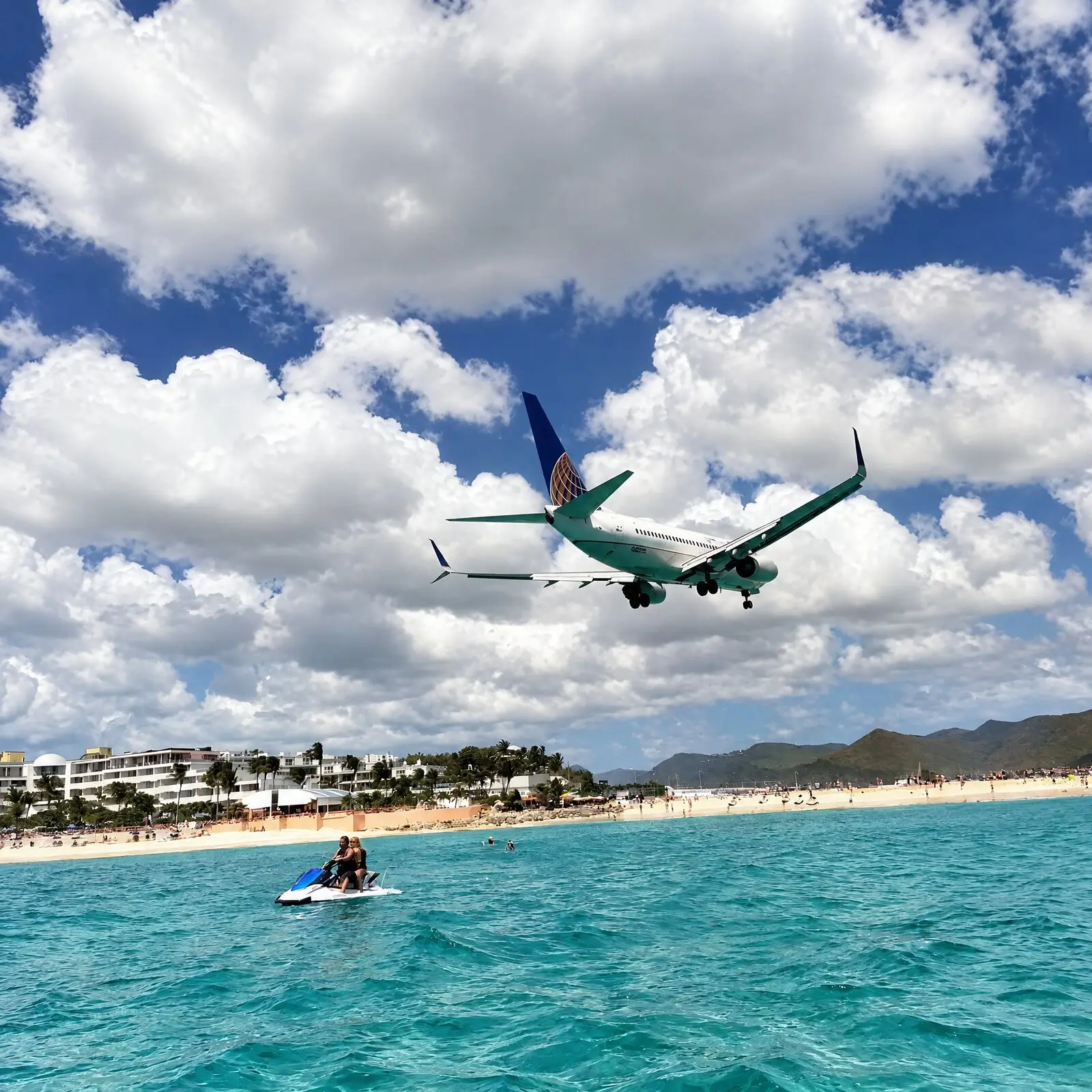 Un avion de ligne passe au ras de la plage de Maho, au-dessus d'un jet ski sur l'eau turquoise