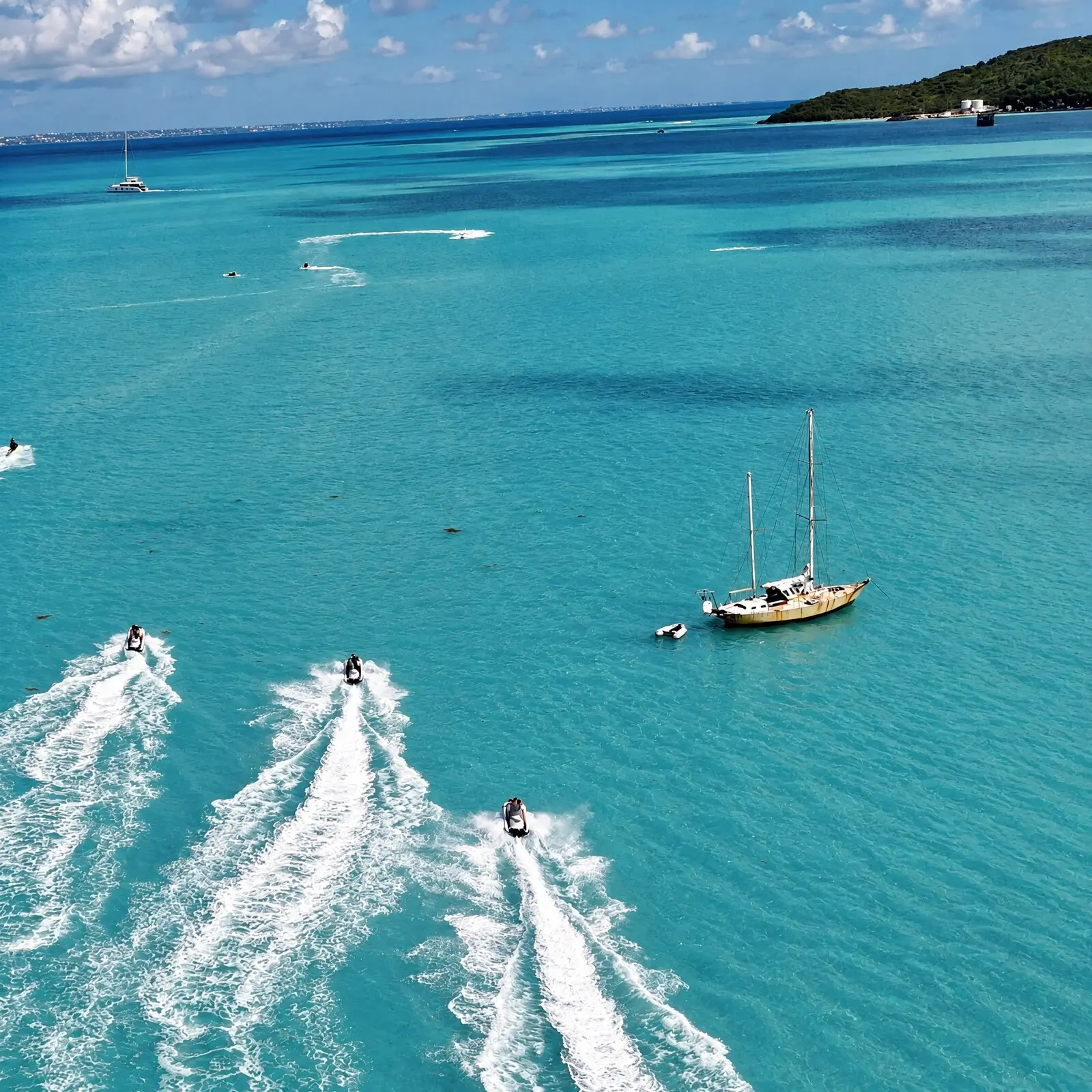 Trois jet skis tracent leur sillage sur l'eau turquoise du lagon de Simpson Bay, des voiliers au mouillage